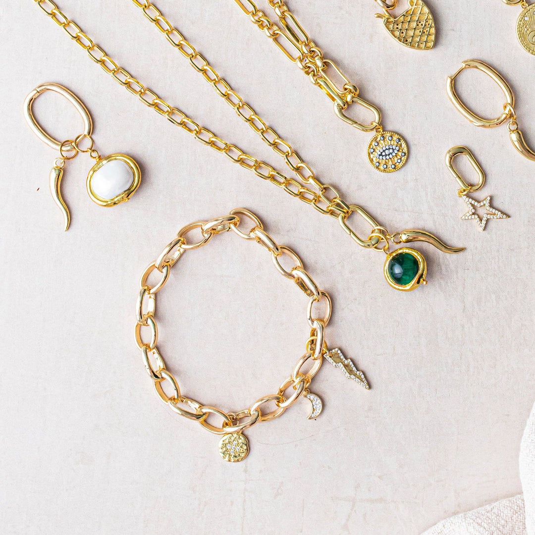 Gold earrings, bracelets & necklaces with charms laid flat on a neutral-coloured background.