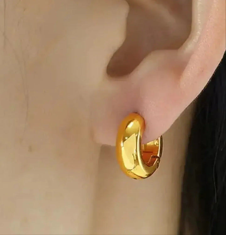 Gold hoop earring worn on an ear with a neutral background