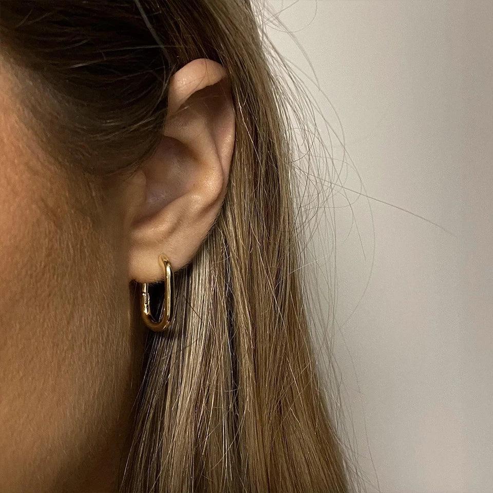 Close-up of an ear wearing a gold hoop earring with a neutral background