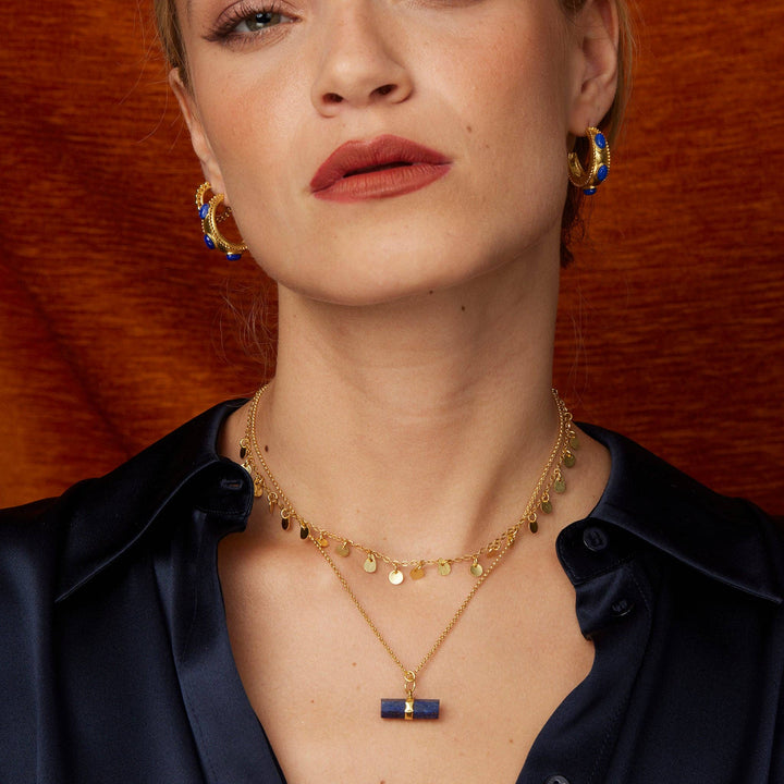 Woman wearing a navy blouse with an open neck showing 2 gold necklaces.