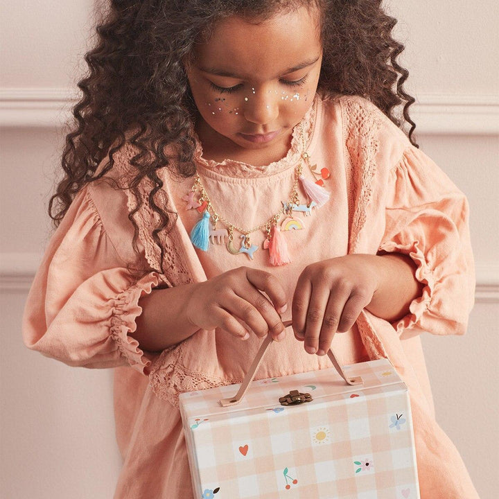 Young girl in a pink dress iholding a advent calendar briefcase wearing an enamel charm necklace