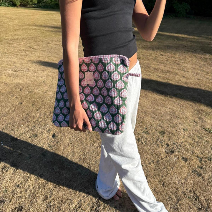 Person holding a patterned clutch bag outdoors on a grassy area