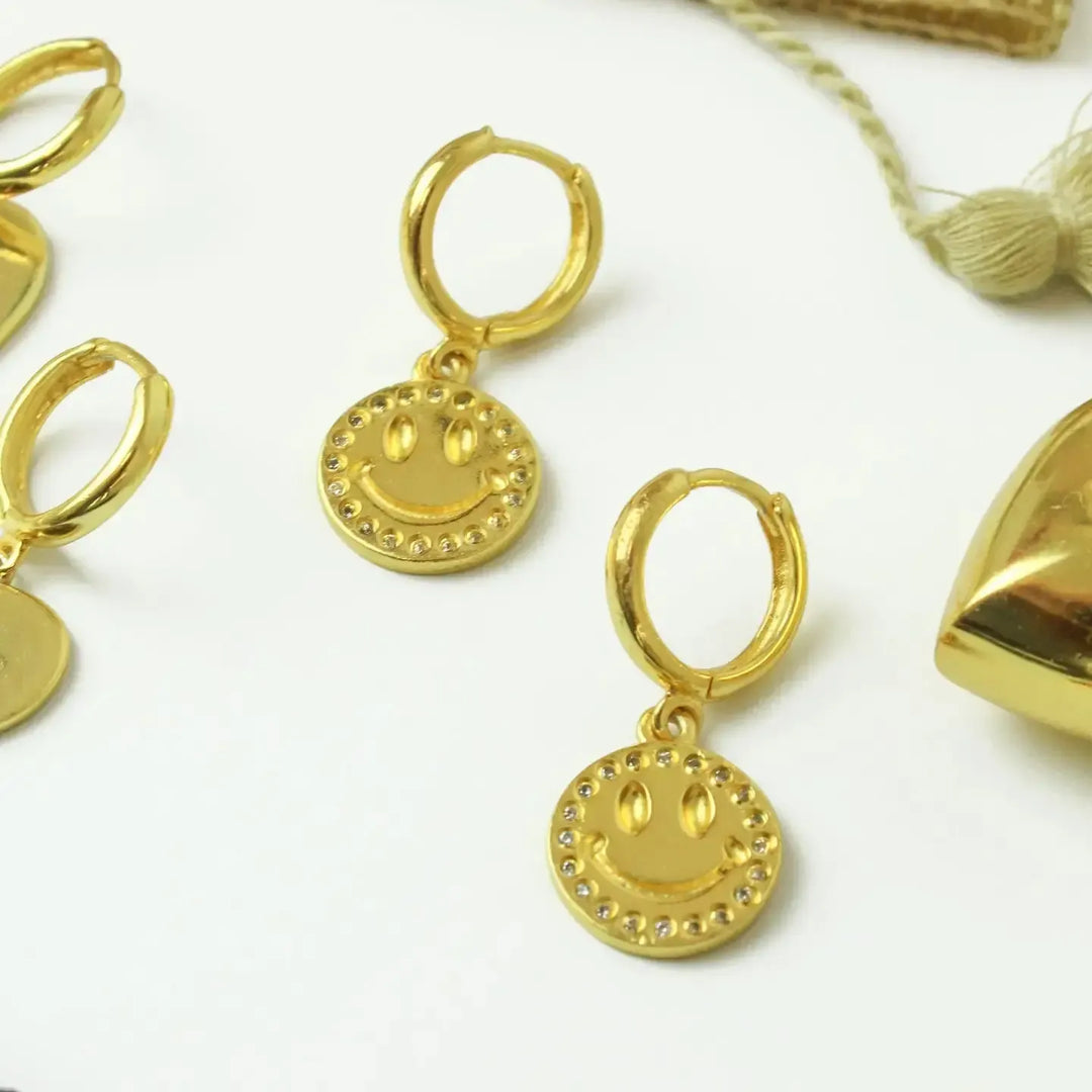 Gold hoop earrings with smiley face charms on a white background