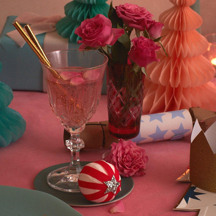Decorative table setting with pink flowers, a glass of pink drink, and festive decorations on a pink surface with peppermint cady striped surprise balls
