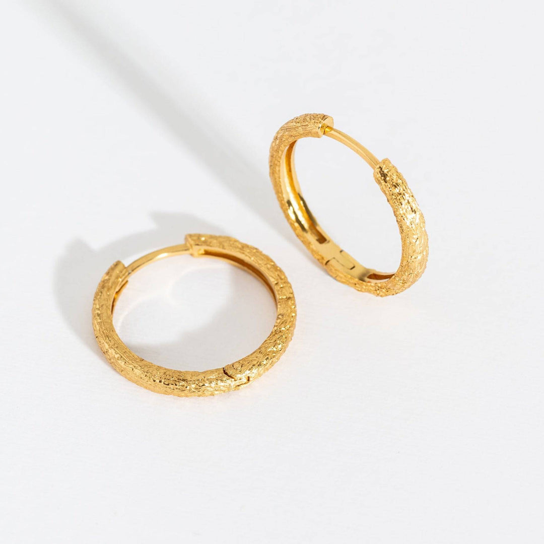 A pair of large gold hoop earrings with antique texture on a white background.