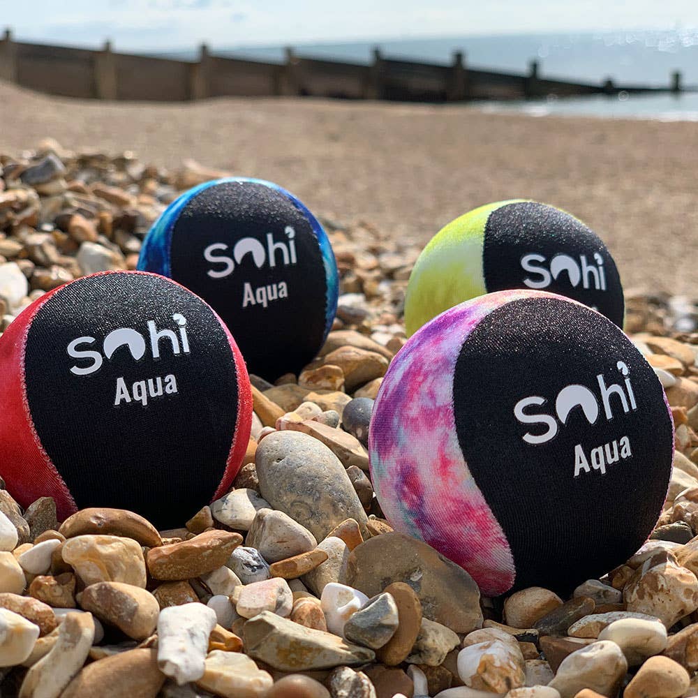 Colorful dog toys with 'Sohi Aqua' branding on a pebbly beach.