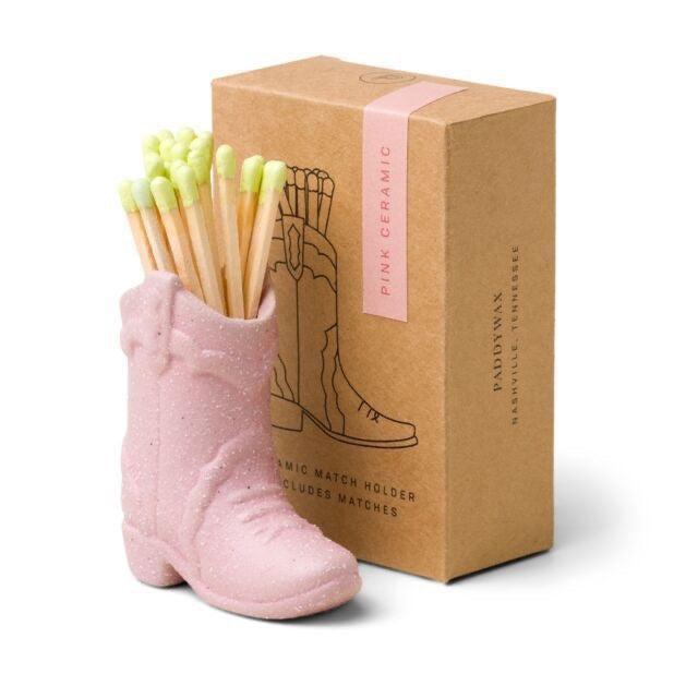 Pink boot-shaped match holder with matches next to a cardboard box on a white background