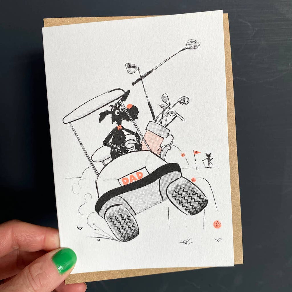 Greetings card with an illustration in black and white of a black dog driving a golf cart with the numberplate'DAD' in pale orange.