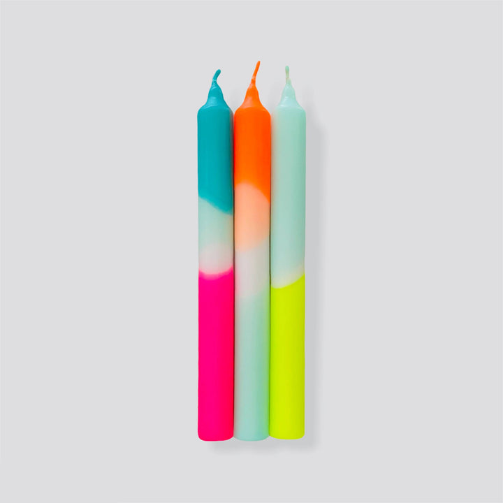 A set of three dinner candles in neon pink, orange, and blue colors, standing upright.