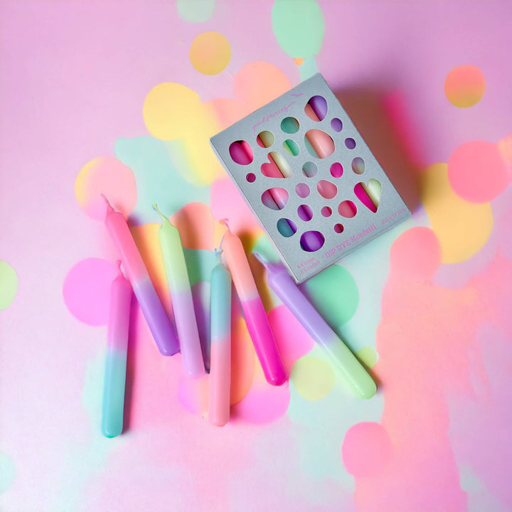 A set of multicolored dip-dye birthday candles displayed on a pink background with colorful bokeh lights.