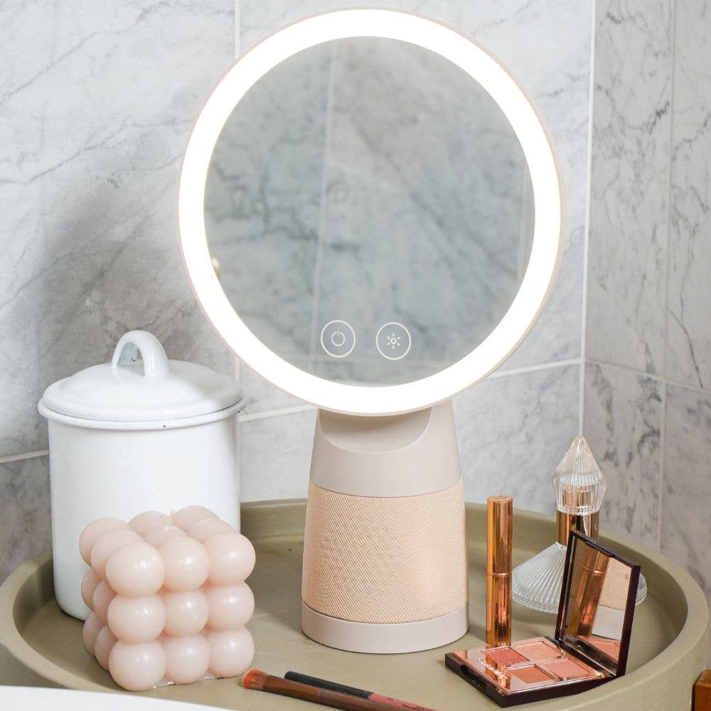 A large makeup mirror with a dimmable ring light in a soft-cream color, accompanied by beauty products on a tray, with a Bluetooth speaker integrated into the mirror's base.