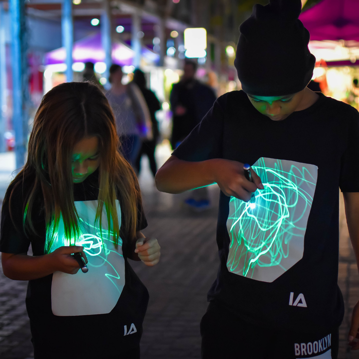 Two children wearing black shirts with glowing designs in a dark setting.
