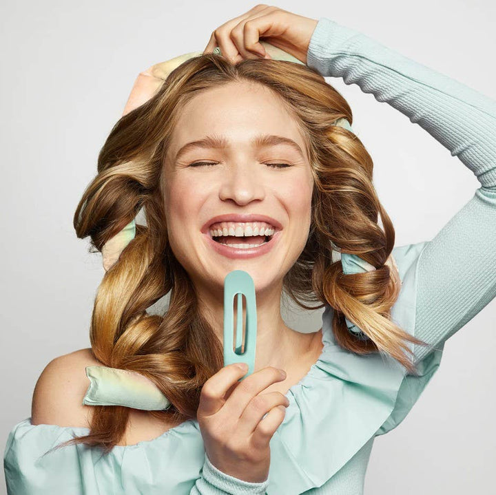 Woman with styled hair holding a hair straightener against a light background