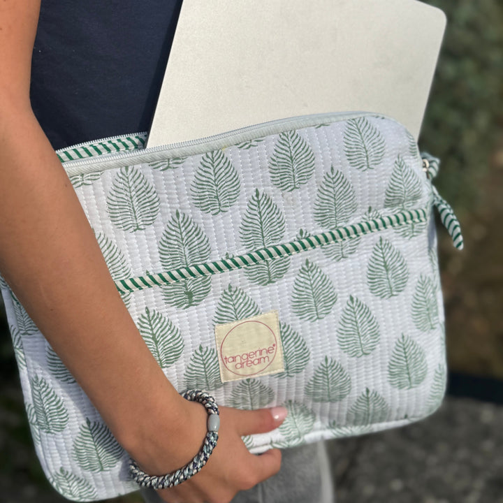 Person holding a laptop in a green leaf-patterned sleeve with a visible brand logo.