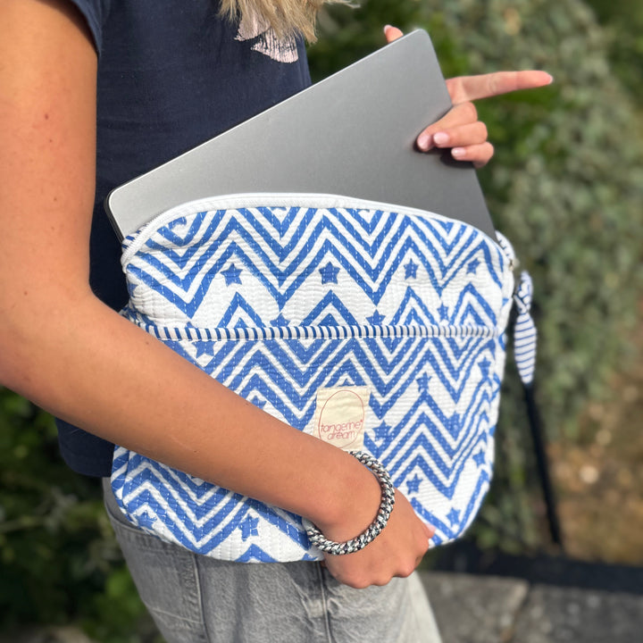 Person holding a blue and white patterned bag with a laptop inside, outdoors.