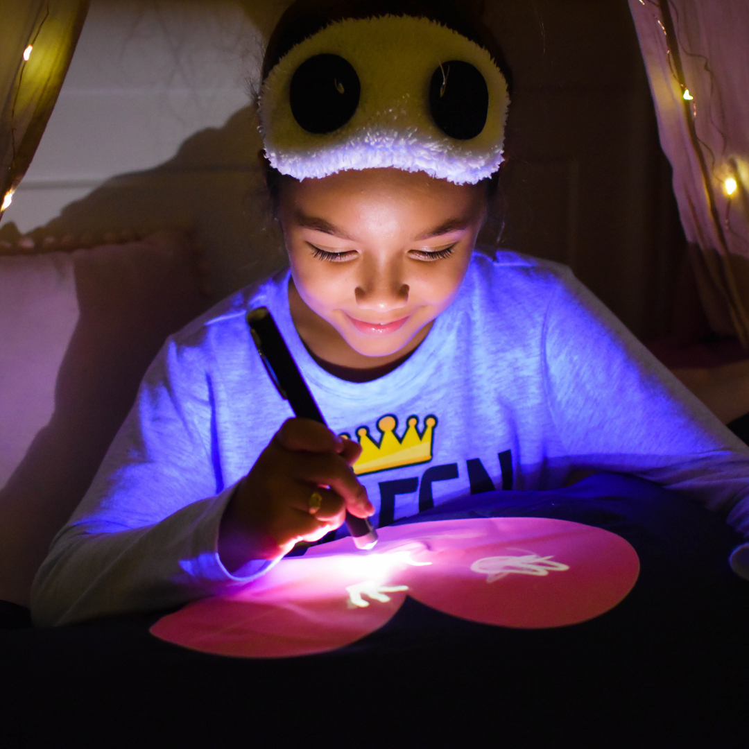 Child using a glowing pen on a dark surface with a soft light source.