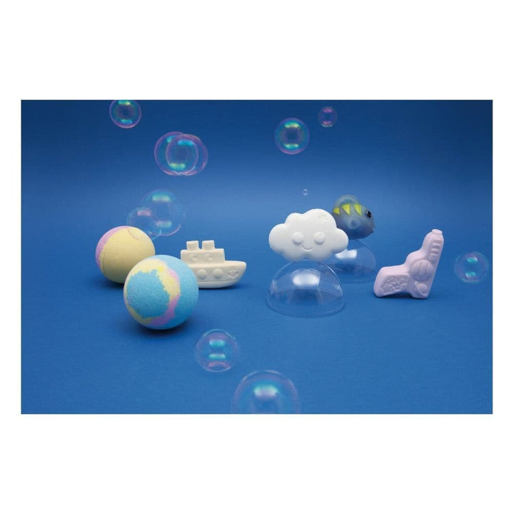 Colorful bath bombs shaped like a cloud, boat, and fish on a blue background with bubbles.
