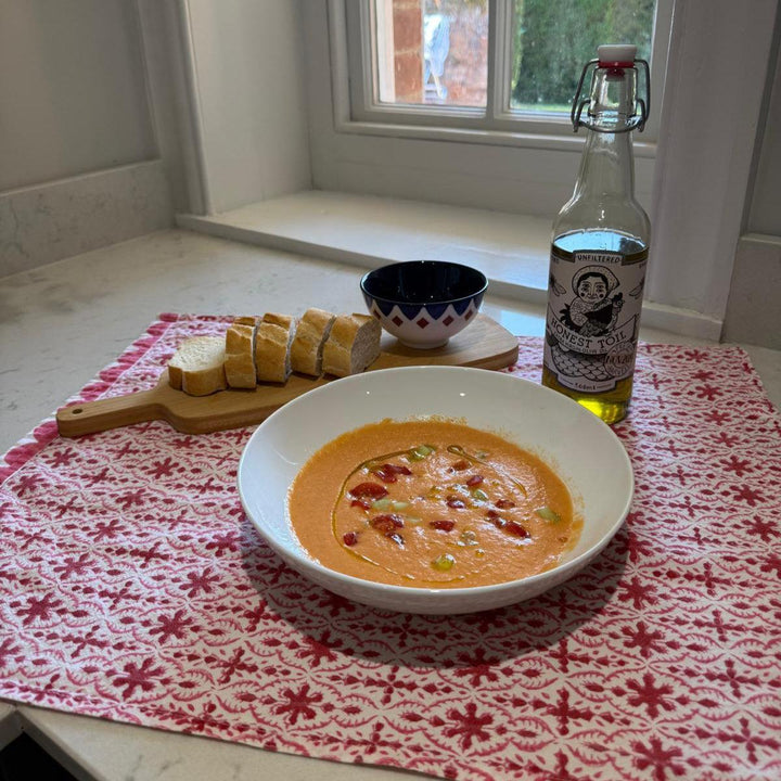 Bowl of soup with bread and a bottle on a table with a red and white patterned tablecloth.