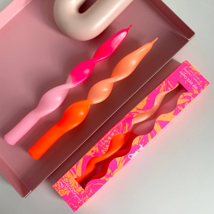 A set of hand-dyed, twisted neon stick candles in pink and orange, displayed alongside their hand-printed packaging.