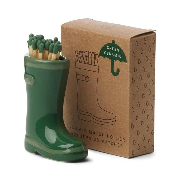 Green ceramic match holder shaped like a rain boot with matches, next to its packaging box.