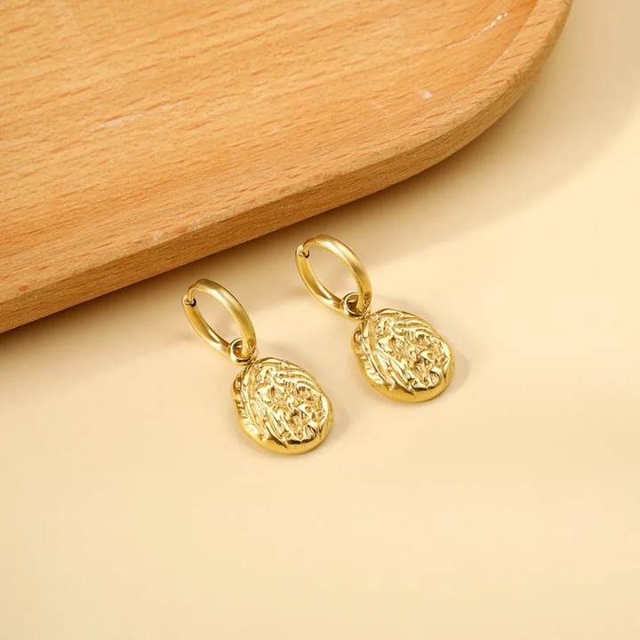 Gold earrings on a beige surface with a wooden background