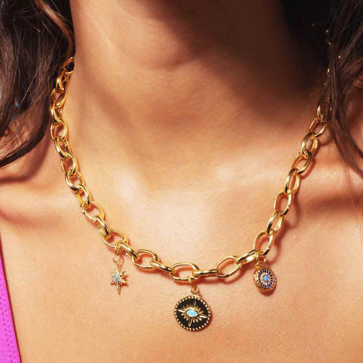 Woman's neck with a chunky gold necklace with three gold charms.