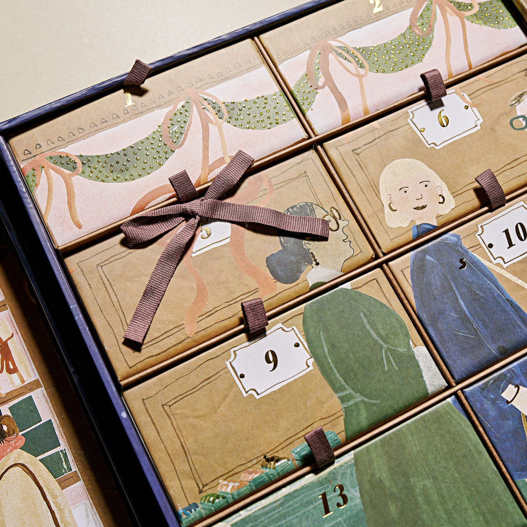 A close-up of the KKNEKKI 2026 Advent Calendar containing multiple illustrated paper drawers with small tabs numbered 1 through 13, tied together with a brown ribbon. The artwork features whimsical figures and garments in muted green, blue, beige, and brown tones.
