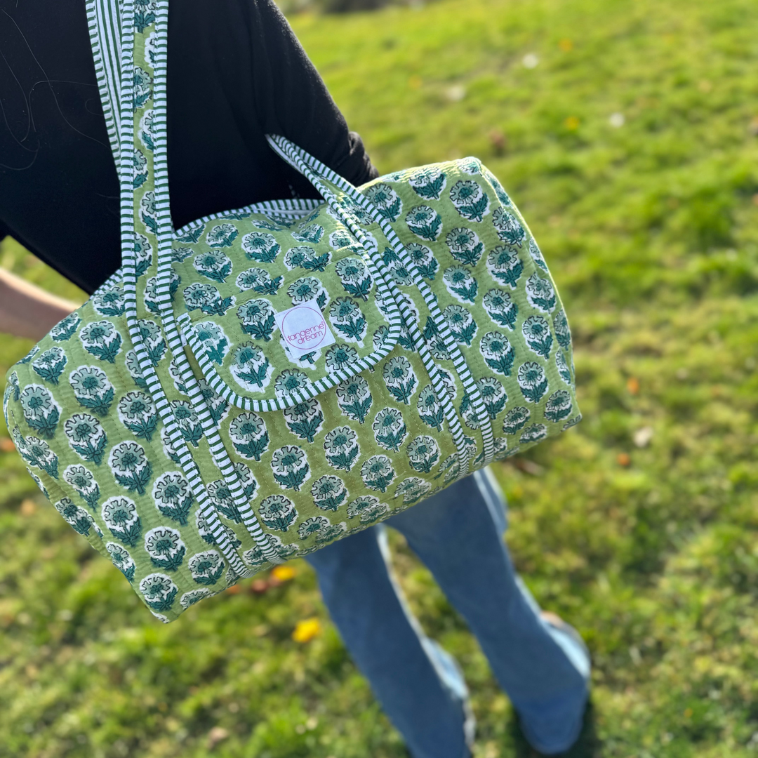 Person holding a green patterned bag outdoors on a grassy field