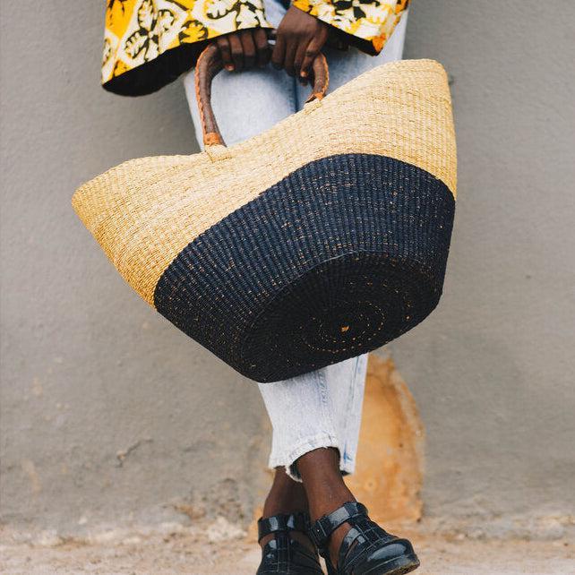 Person holding a straw bag with black bottom half against a neutral background