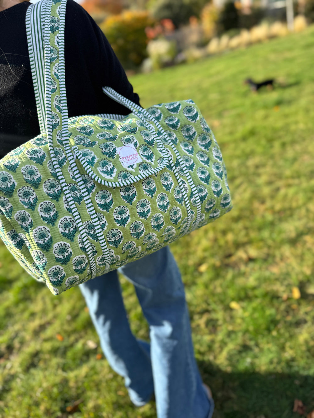 Person holding a green patterned bag outdoors on a grassy area