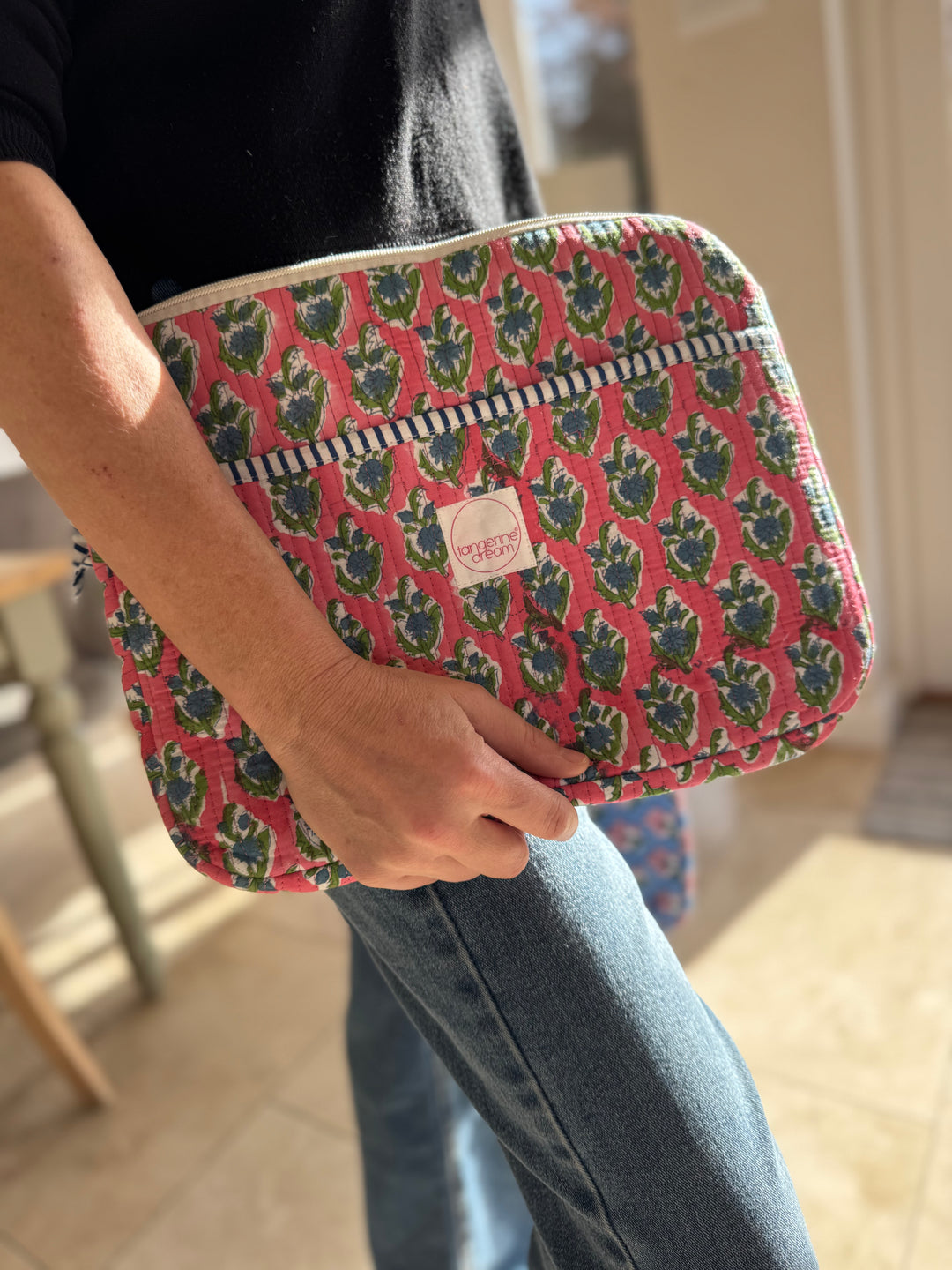 Person holding a pink floral patterned pouch with a visible brand logo.