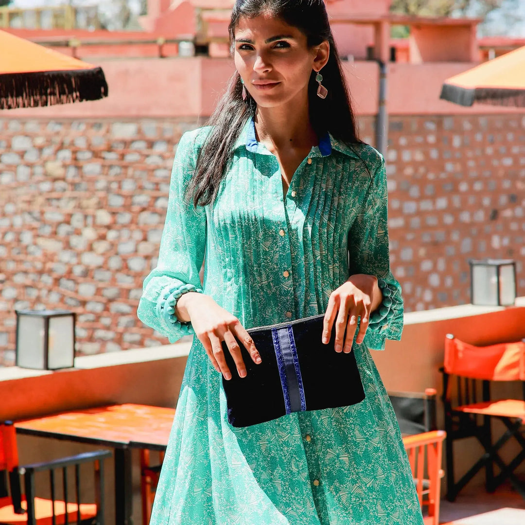 Woman in a green dress holding a black clutch on a rooftop with red brick walls and orange chairs.