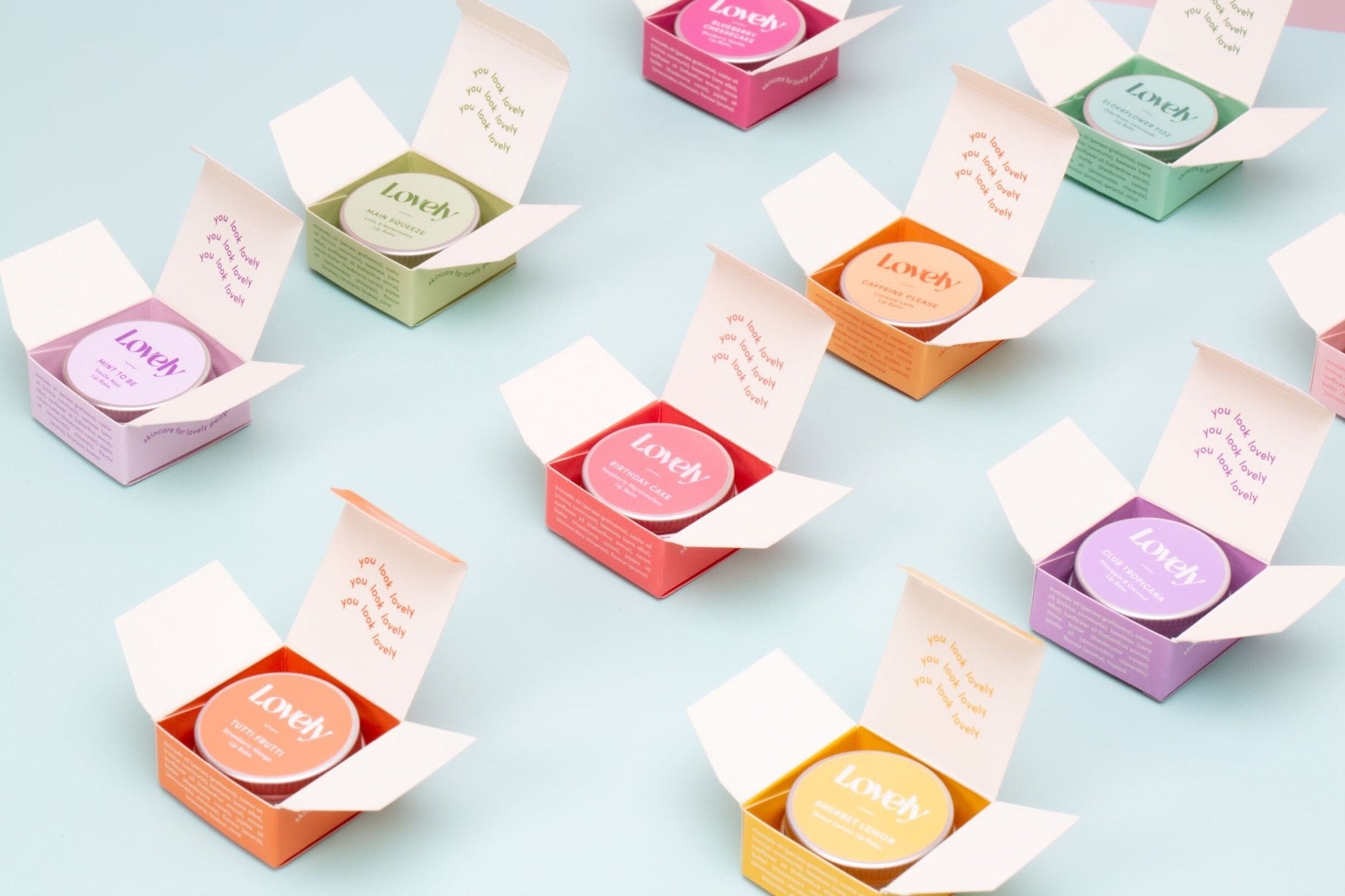 Flavoured lip balm tins in pastel-coloured open boxes arranged diagonally.