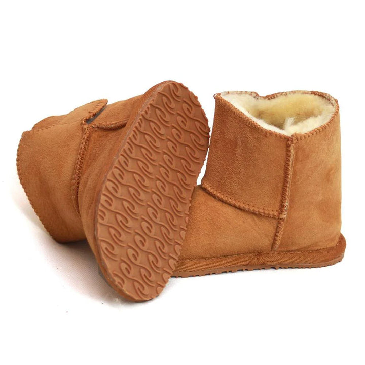 A pair of tan-coloured sheepskin baby boots with one boot on its side to show the patterned sole.