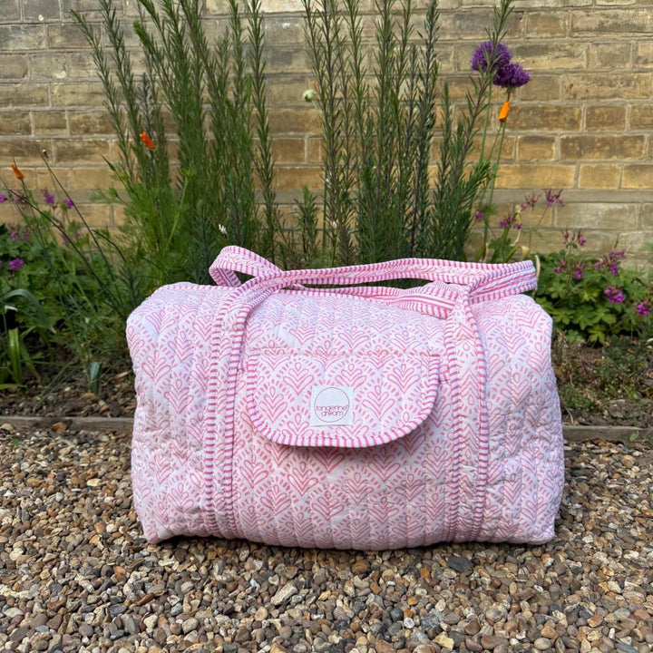 Pink textured bag on a pebbled surface with a garden background