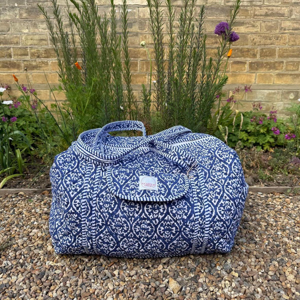 Blue patterned bag on a pebble surface with plants and flowers in the background