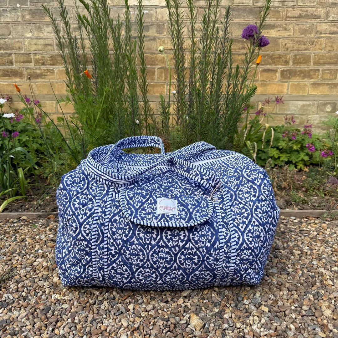Blue patterned bag on a pebble surface with plants and flowers in the background