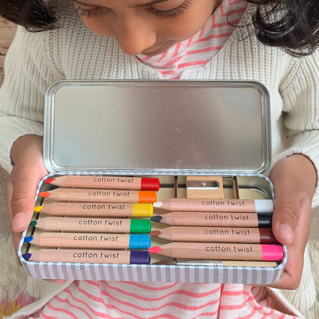 Girl looking down on a tin holding jumbo coloured pencils with a sharpener.