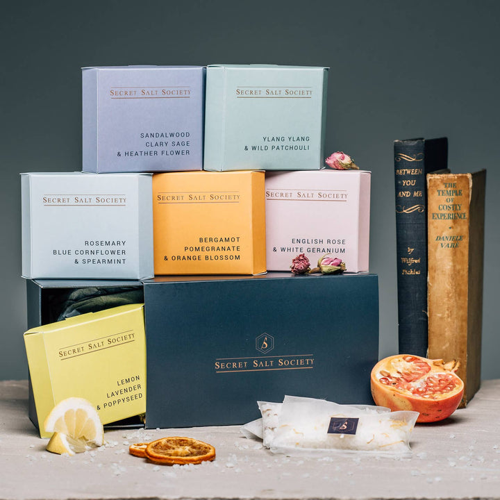 Pastel-coloured boxes with gourmet salt from Secret Salt Society arranged in  a still-life set-up with old books and half a pomegranate.