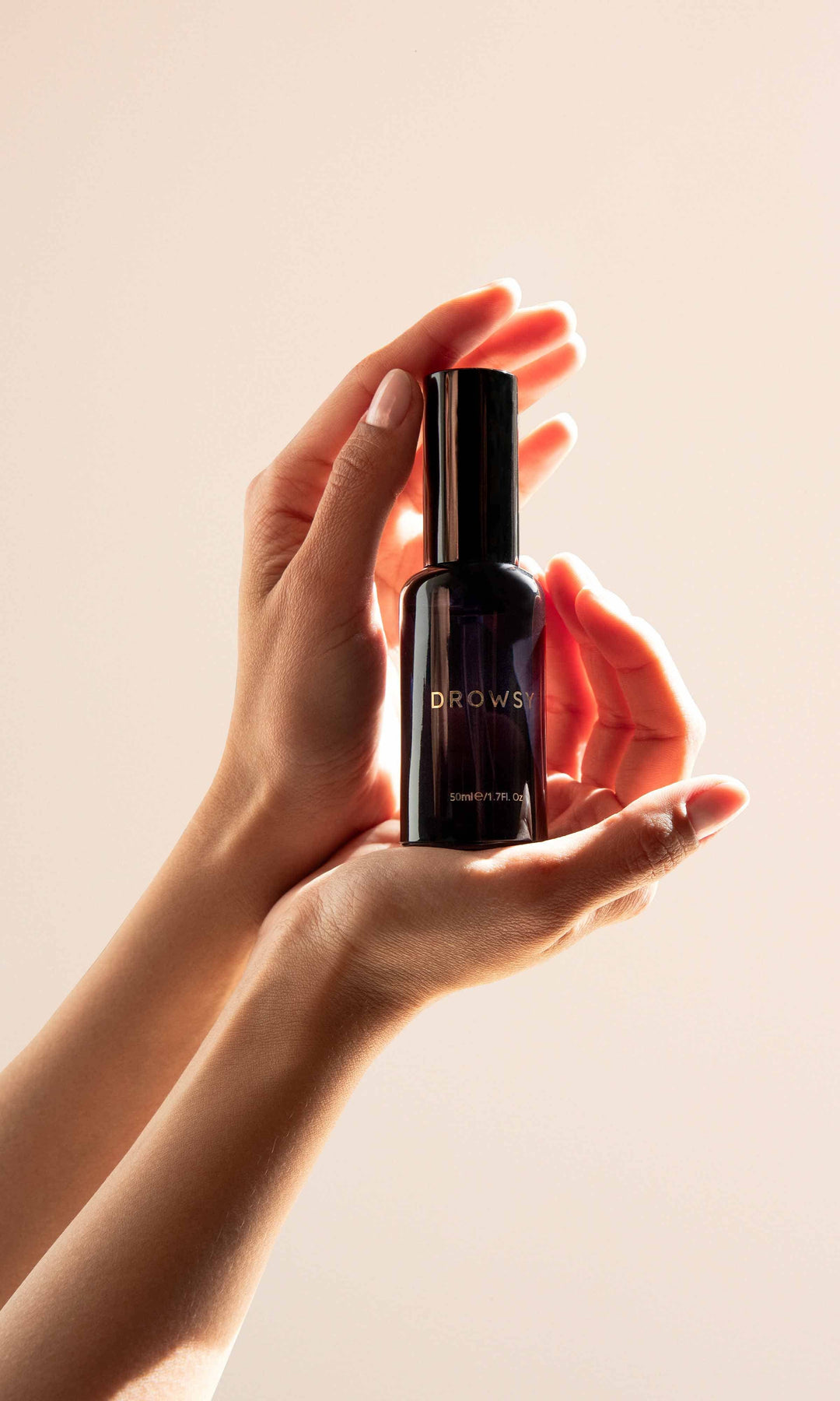 Hand holding a black bottle labeled 'Dior' against a beige background